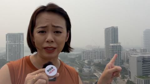 Tessa Wong wearing an orange singlet pointing to the Singapore skyline behind her.
