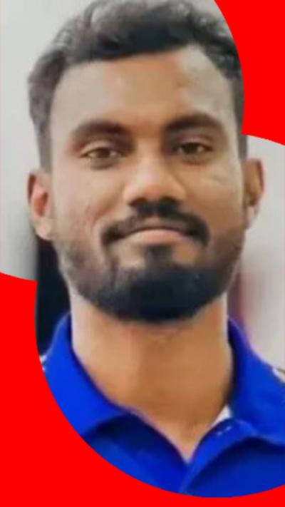 A man with a full beard and moustache looks directly at the camera. He is wearing a bright blue open-necked shirt. 