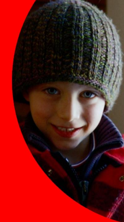 A young boy wearing a wooly hat and coat smiles into the camera.