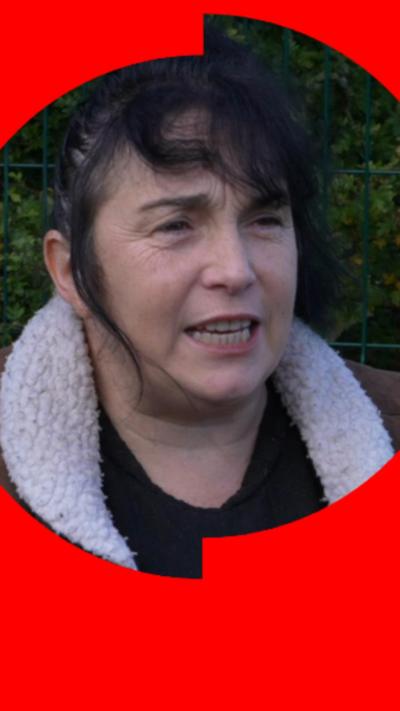 A woman with black hair wearing a woolly-collared coat and looking off camera.