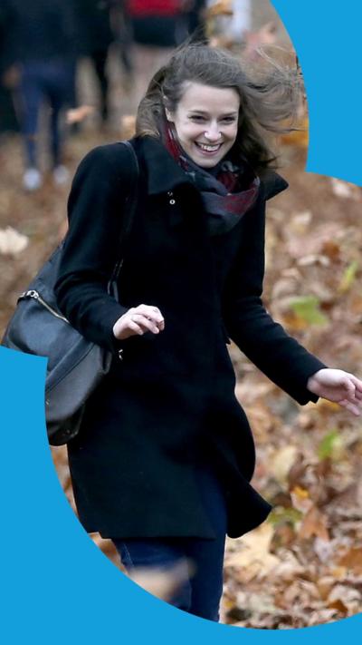 A woman wearing a dark blue coat smiles as she battles the wind