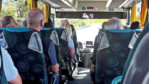 A photo showing the inside of a coach, and the backs of passengers' heads as they sit in their seats. Some are looking out the window.