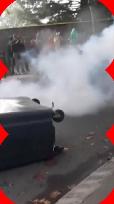Riots on the streets of France with a bin on the floor with smoke behind it
