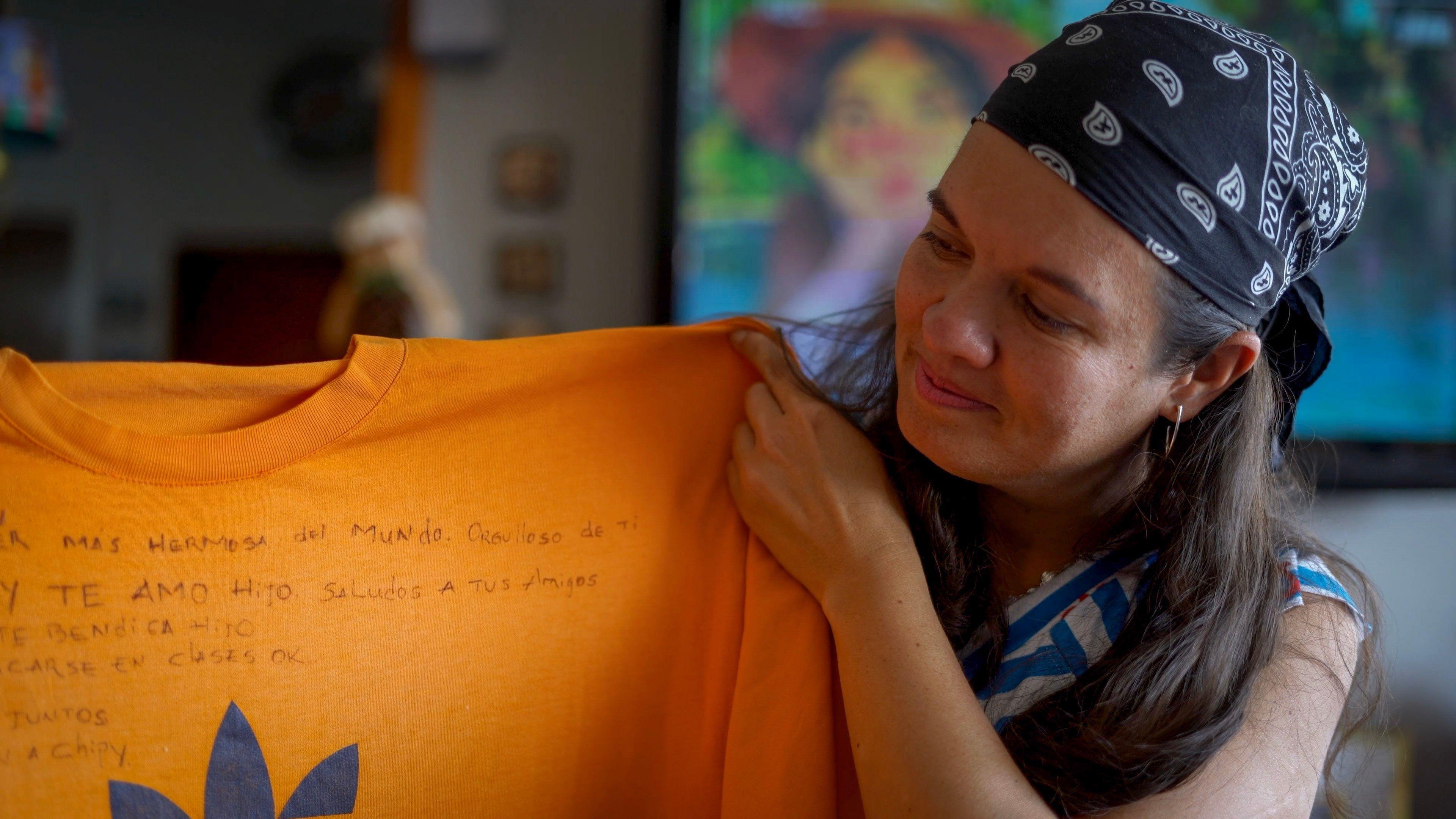Angel Godoy's wife hold up an orange T-short with writing on it, a message her husband scrawled on it while he was in prison in Venezuela
