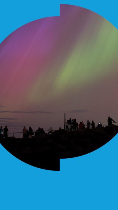 A group of people are silhouetted against the night sky with the lights of the aurora above them.