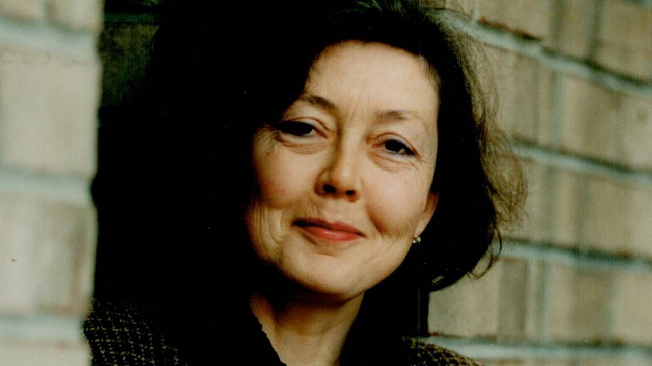 Anne Carson smiling against a brick wall
