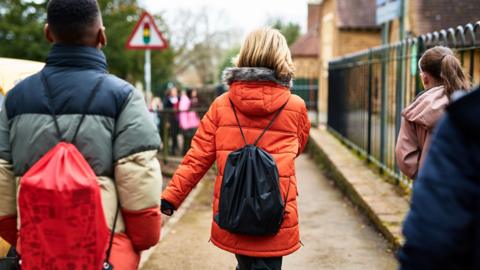 Three children walking down the road to a school, wearing coats