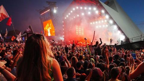 Crowd of people face the Pyramid stage at Glastonbury Festival as darkness falls