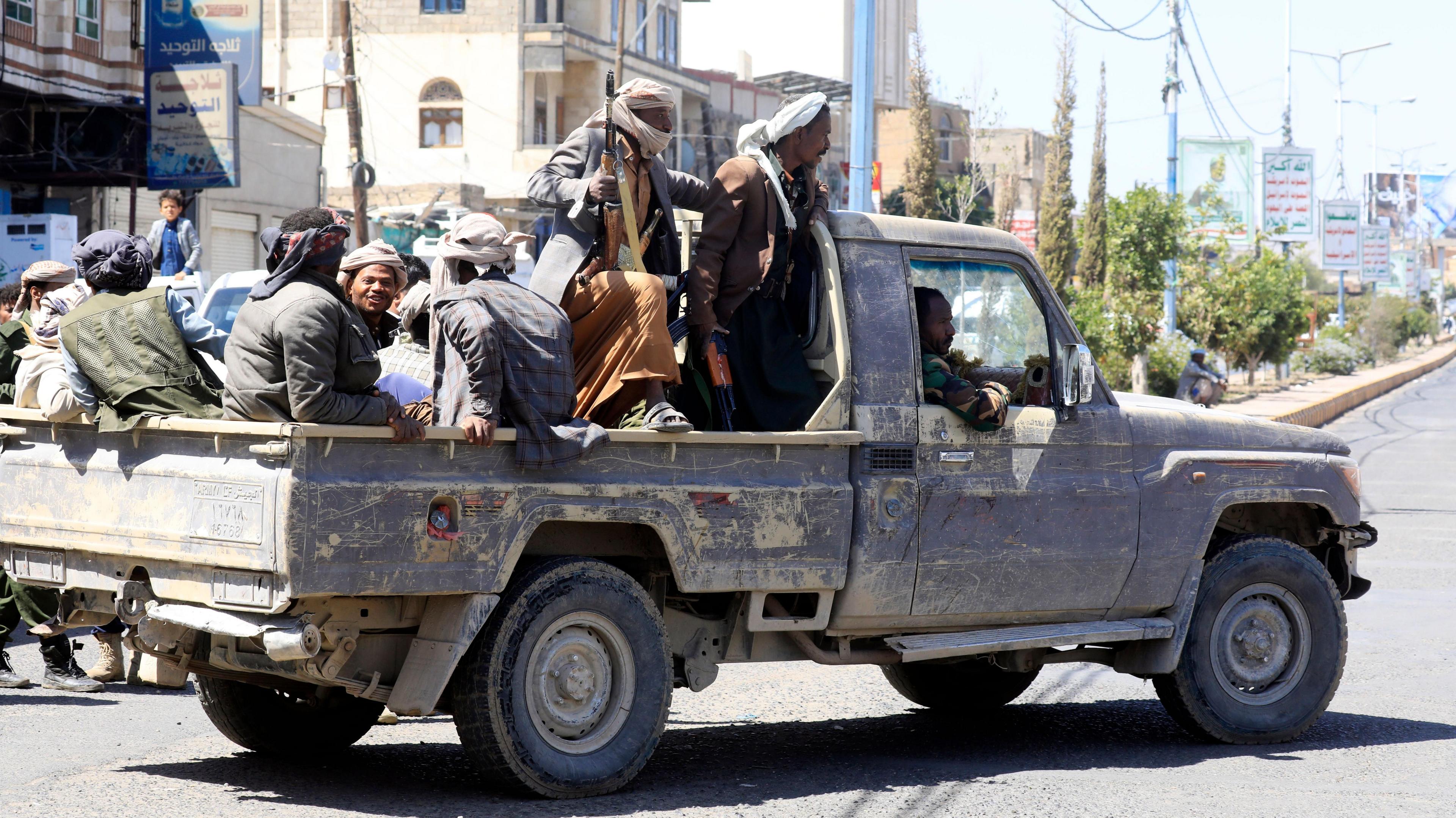 Houthi fighters seen riding in the back of a pickup truck, with some men holding guns.