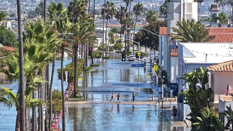 People walk near coastal floodwaters amid strong waves and high tides generated by Tropical Storm Rachel on October 9, 2026 in Newport Beach, California.