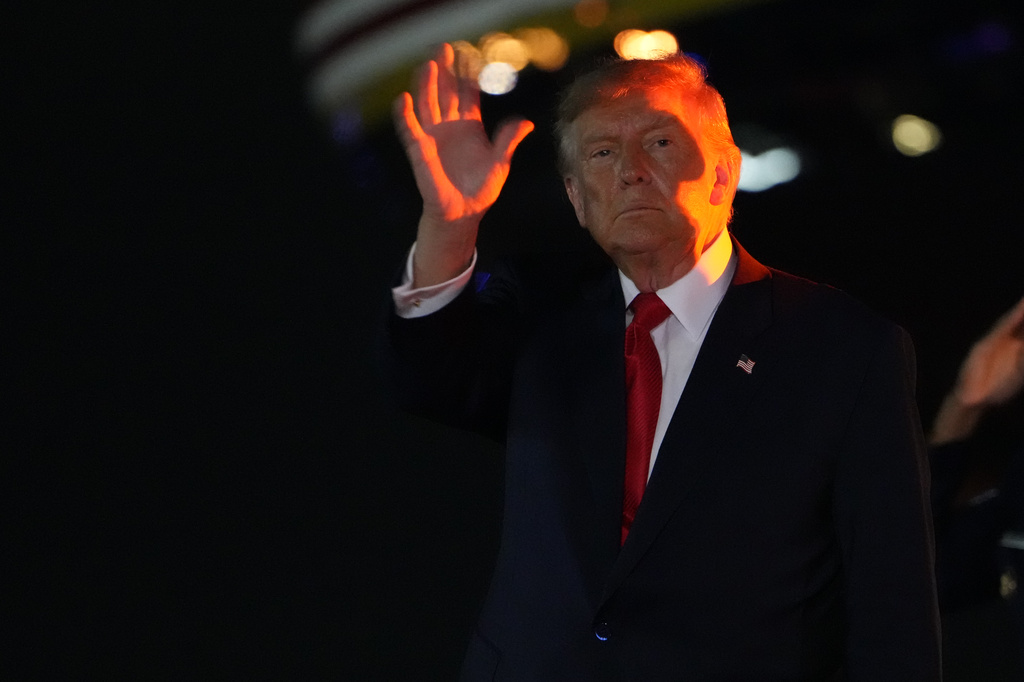 trump waves in the nighttime with a red light shining on him