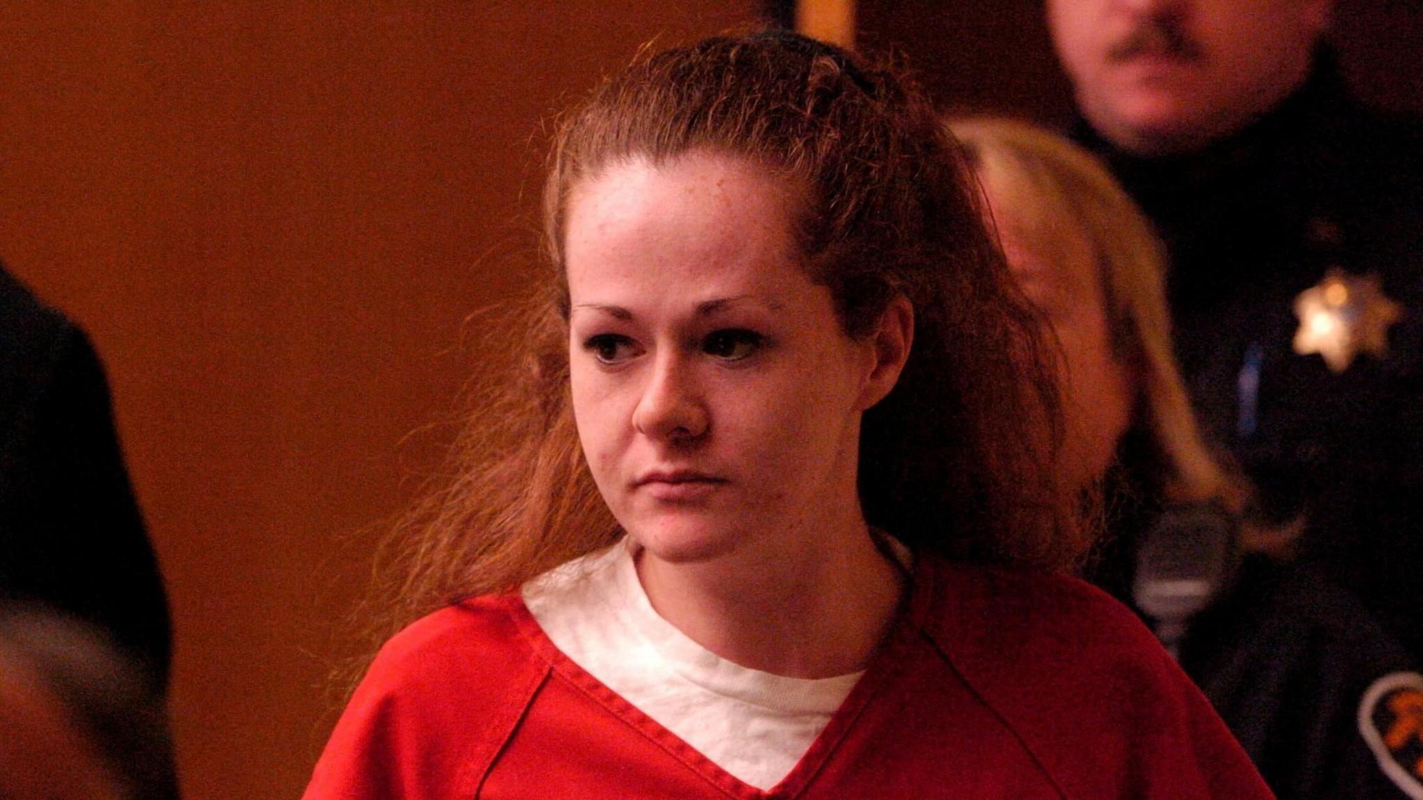 Christa Pike, a woman with red hair wears a white top with a red top on top