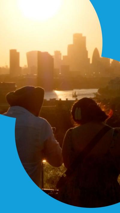 Two people are stood watching the sun set. They are looking out over a city skyline.