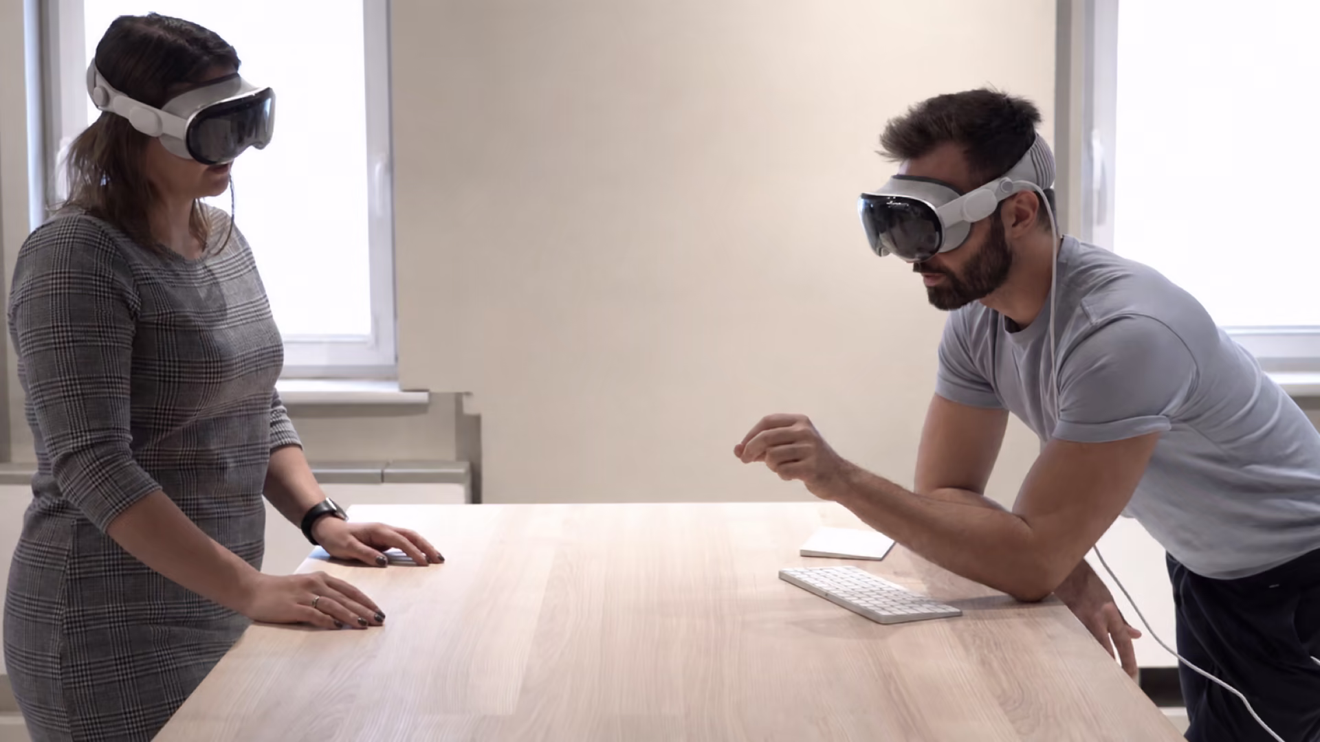 Two people across a desk each wearing a Vision Pro, with no virtual content rendered