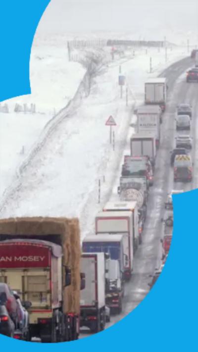 Traffic queues on a motorway with snow-covered fields either side.