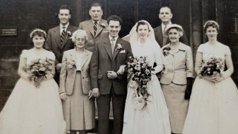 A black and white picture of a bride and groom on their wedding day with two bridesmaids and several other people.