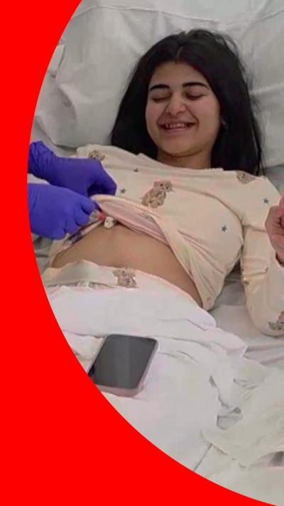 A young girl is laid in a hospital bed being tended to by a nurse wearing gloves.