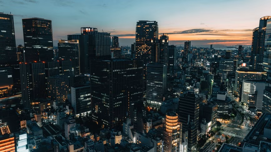 Office towers and streets in Umeda, Osaka, at dusk, with lit windows and an orange sunset over the bay