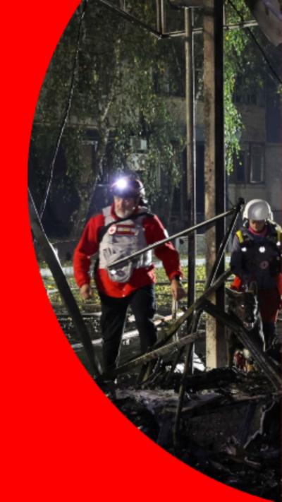 A man wearing a helmet with a torch attached stood on top of a demolished structure at night time.