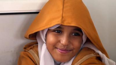 A young Yemeni girl wearing a hood and head scarf smiling 