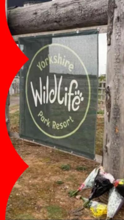 A green sign reading 'Yorkshire Wildlife Park Resort' with flowers laid at the foot of the sign post.