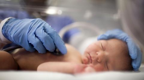 Image showing a newborn baby lying down with the soles of their feet in the foreground. The baby is wearing a nappy with a tag attached to one leg.