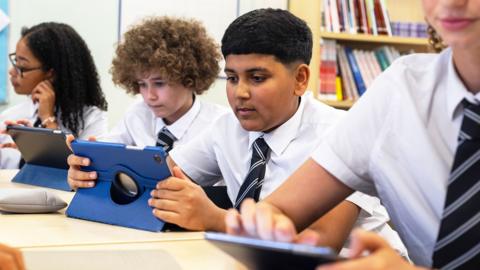 Teenage students in school uniform using touchscreen tablets in the classroom