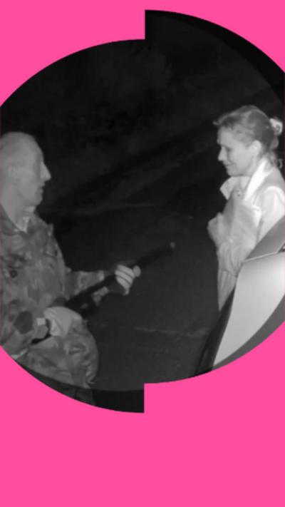 A black and white CCTV image of a man (left) pointing a shotgun at the chest of a woman (right).