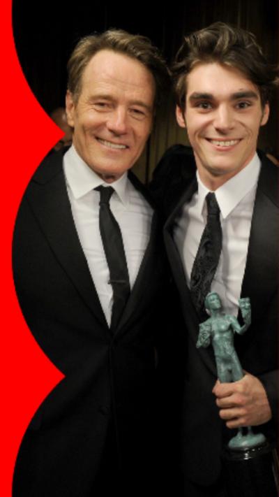 Bryan Cranston (left) and RJ Mitte (right) both are holding green trophies and both are wearing tuxedos.