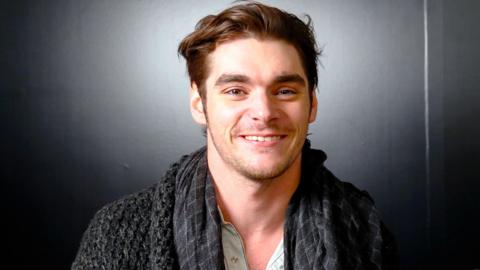 RJ Mitte smiling and wearing a grey cardigan 