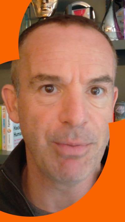 Martin Lewis looks straight ahead at the camera. Only his face and neck is visible and he is in front of some shelves with books on.