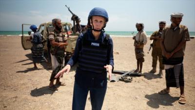 A woman wearing a bullet proof press vest in the middle of a desert in Yemen