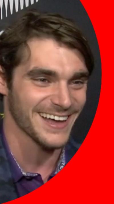 Image of actor RJ Mitte, with short dark hair. He is wearing a blue jacket over a purple shirt.
