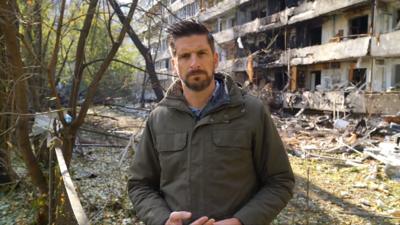 Dan Johnson standing in front of an apartment block that was hit by a Russian missile attack.