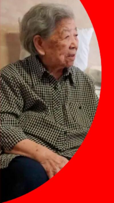 An elderly woman with short grey hair, wearing a black-and-white checked shirt