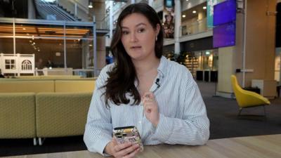 Woman with brown hair wearing a blue and white striped shirt holding a phone