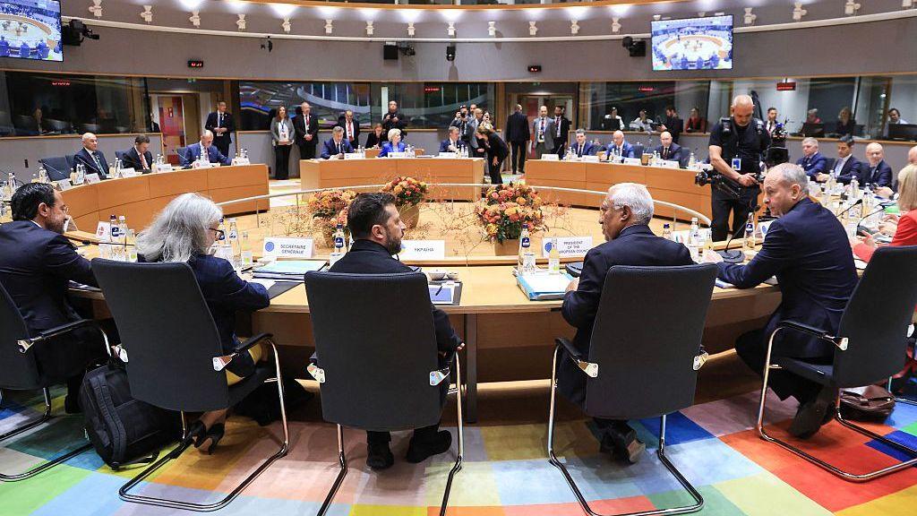Zelensky sitting with other EU officials at a huge round table.