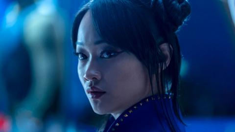 A close up shows Callina Liang as Chun-Li, her hair tied half-up, looking sideways at an object or person of interest off-screen. The shot has a blue hue, giving it a moody, threatening feel.
