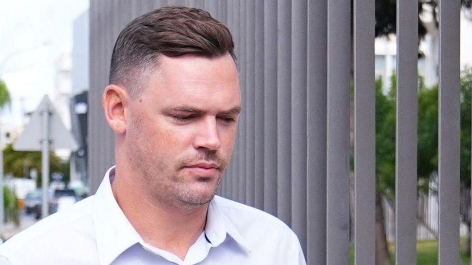 Joshua Foster wearing a white shirt as he arrives at court in Cyprus. He has short dark hair.