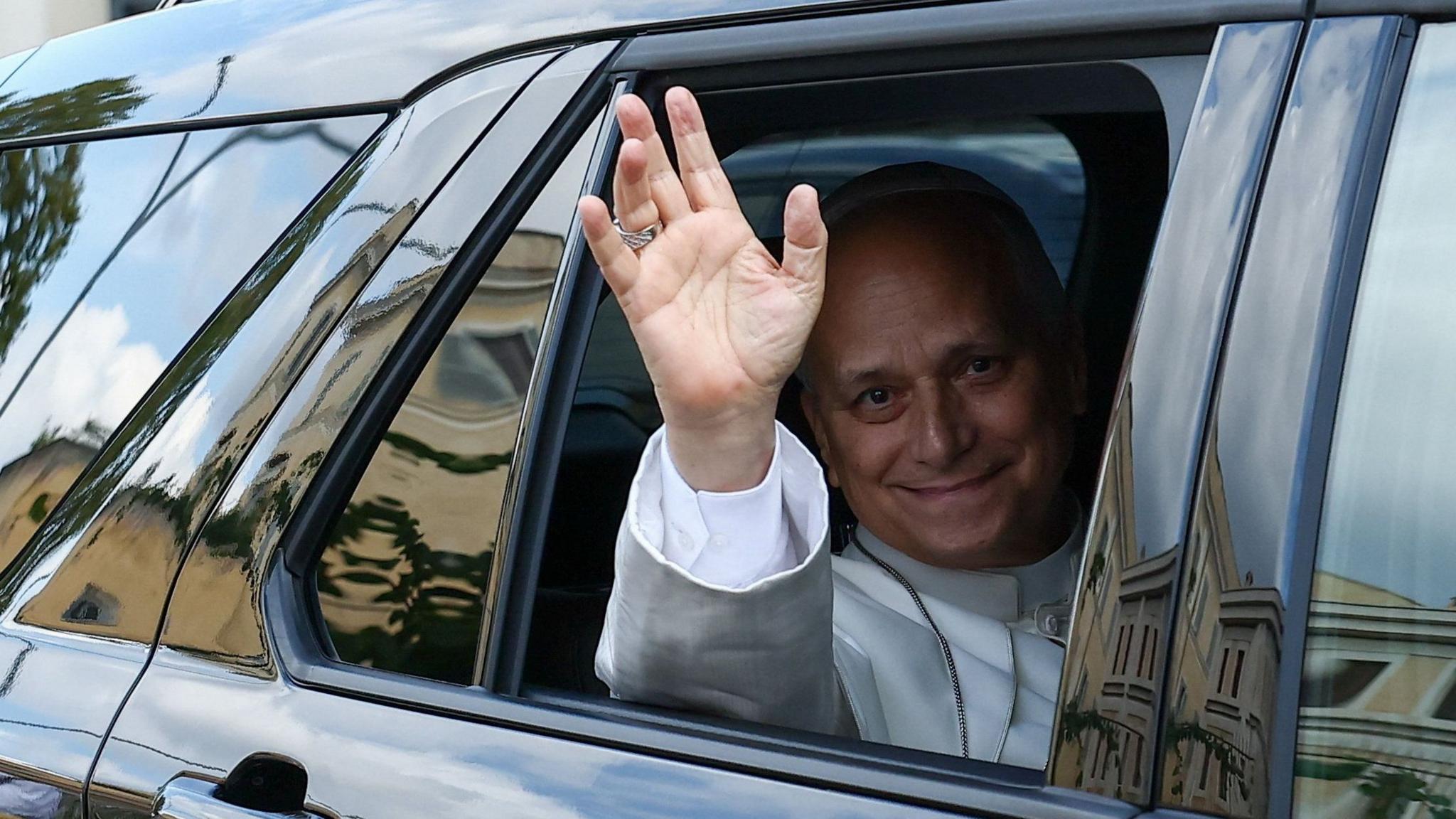 Pope Leo XIV waves from the window of a car as he leaves Rome's Gemelli University Hospital.