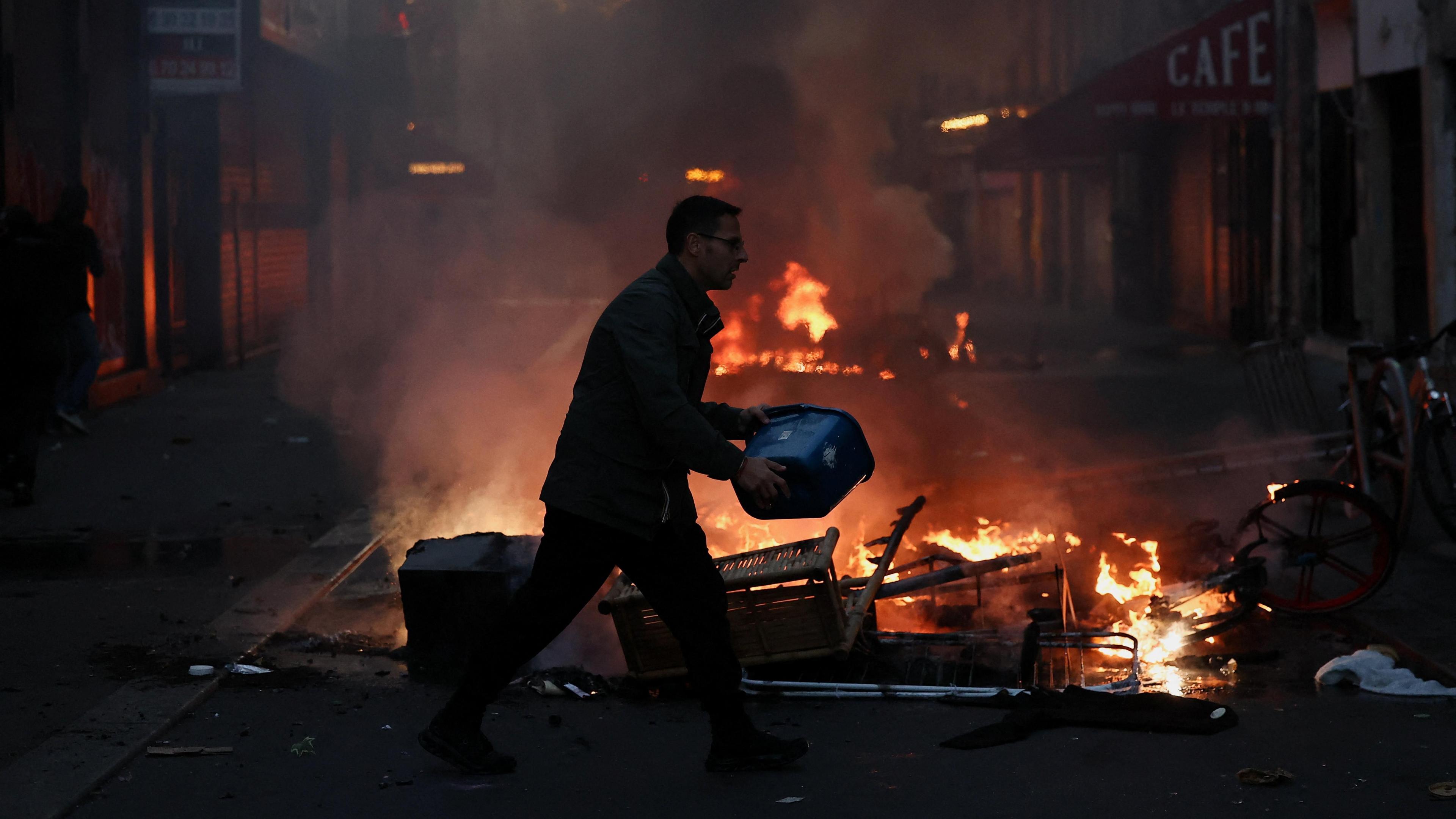 A man tries to extinguish a fire, during civil unrest, the day after a national day of demonstrations against the cost of living and rising fuel prices, in Paris, France, October 18, 2026.