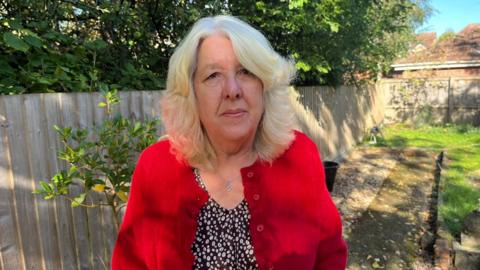 A woman wearing a red cardigan, she has blonde hair 