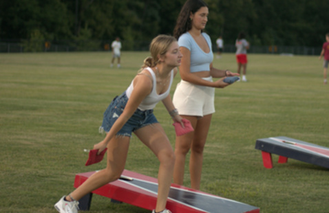 Two student playing cornhole and one about to toss a bag
