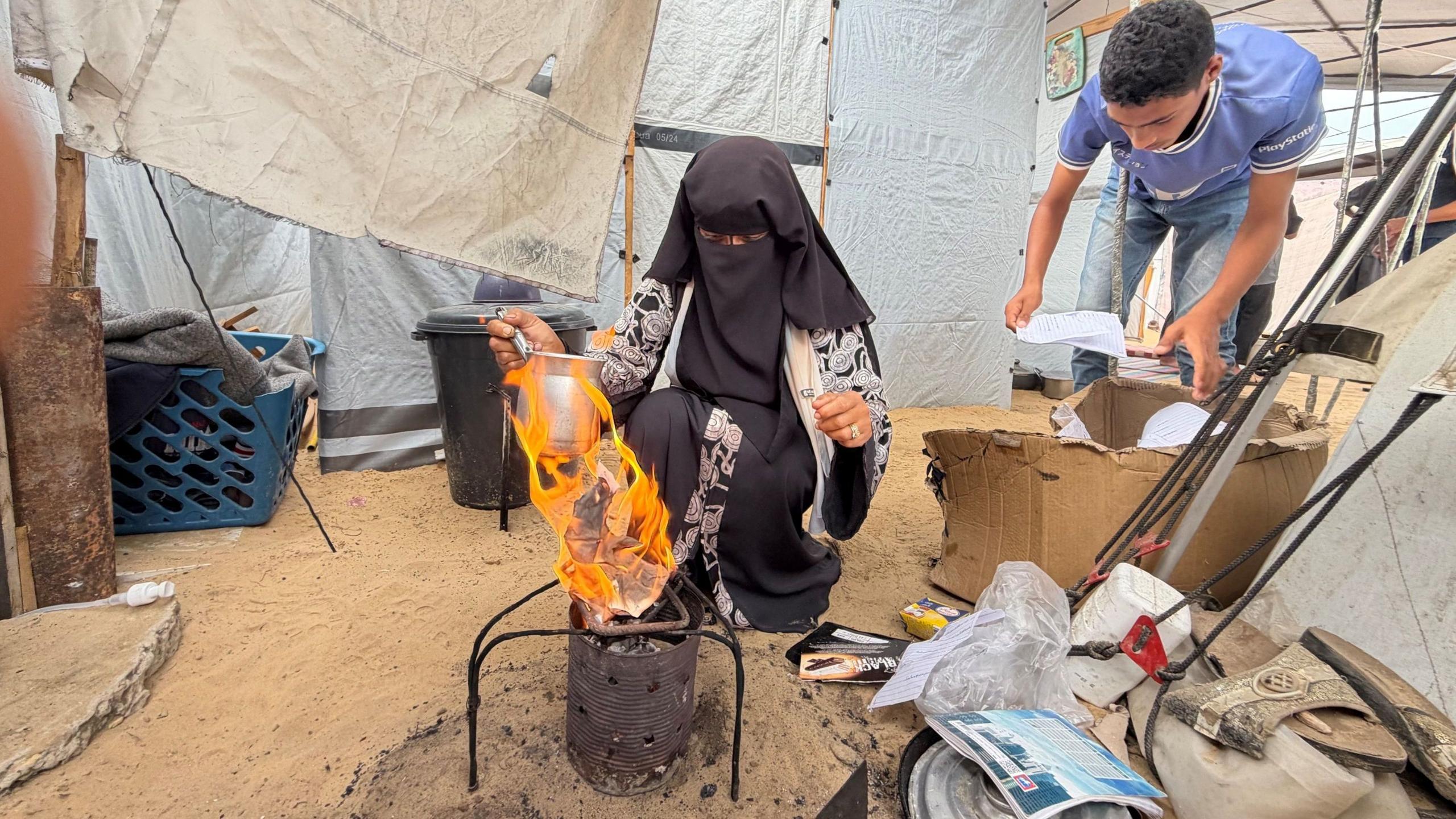 Sawsan Bahloul sets fire to paper and cardboard to heat a pot, outside a tent in Gaza