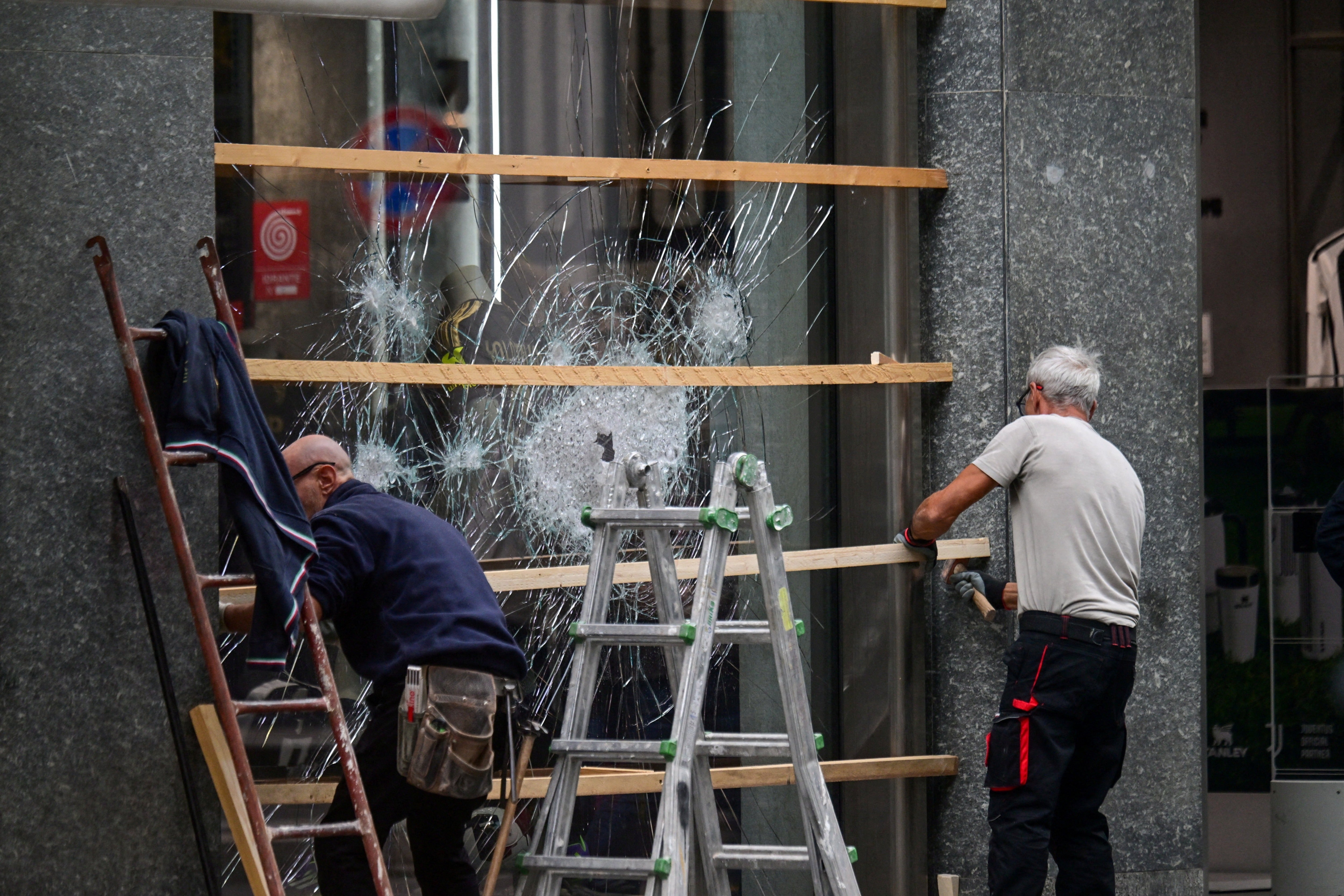Workers secure a shattered shop window with wooden boards following clashes between police and protesters