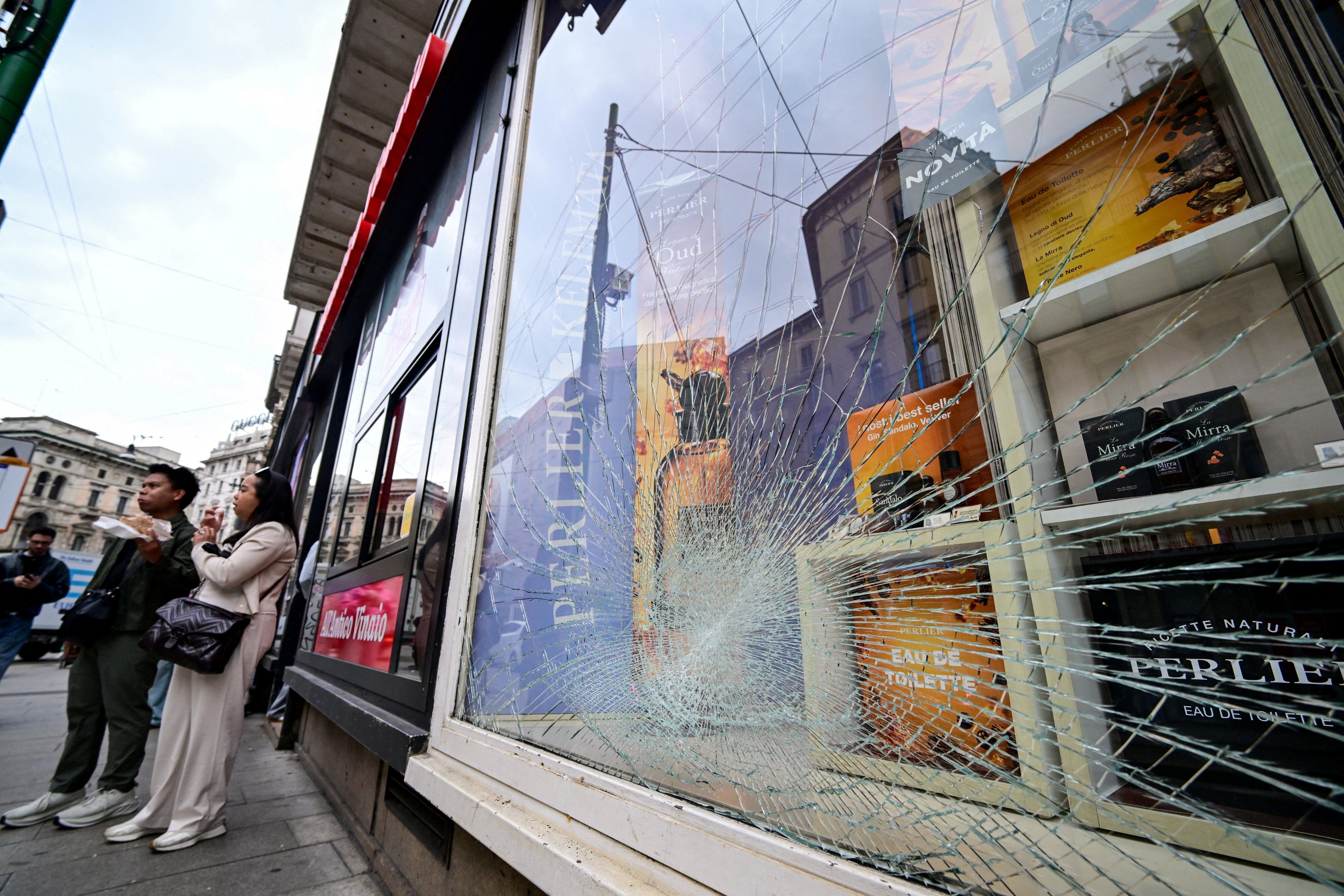 A shattered shop window is seen as pedestrians stand nearby