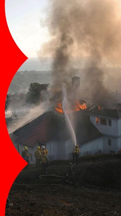 Thick black smoke billows out of the roof of a home on fire in California