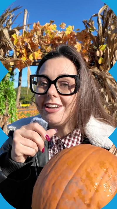 A woman with brown hair and glasses holds a pumpkin