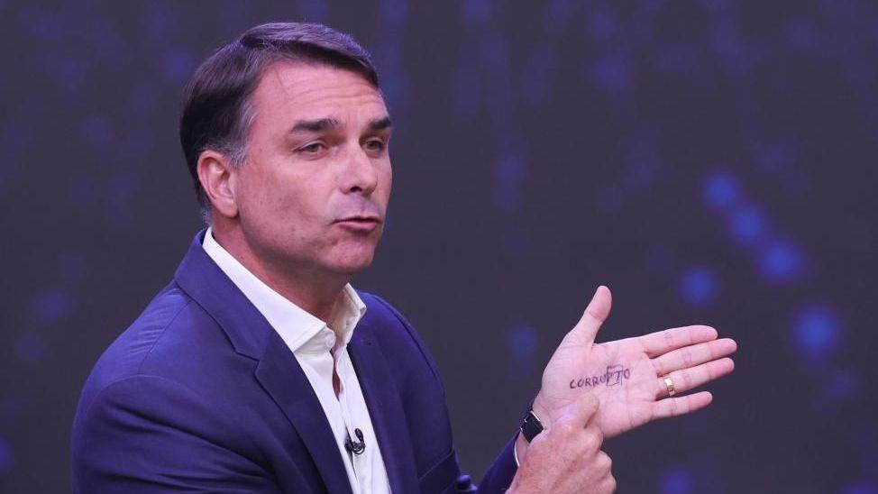 Bolsonaro points with one finger to the word "CORRUPTO" scribbled on his hands. The letters "p" and "t" are surrounded by a square. 