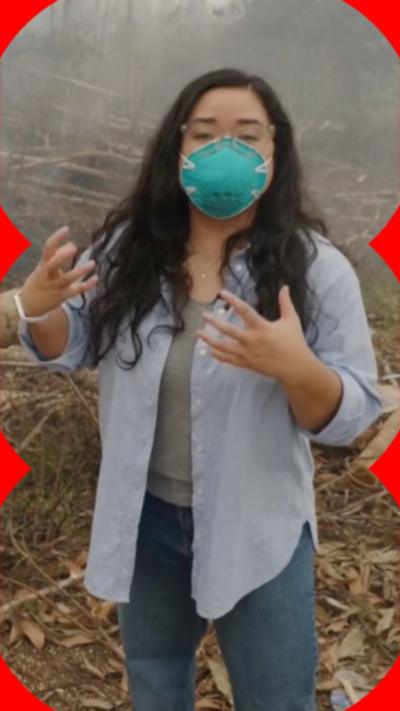 A woman stands looking at the camera wearing a protective mask.